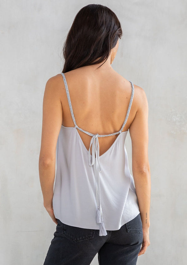 [Color: Platinum] A model wearing a Holiday ready silver grey camisole. For your next special occasion, featuring a ruffle trimmed front and a beaded accent neckline with long beaded straps that tie in the back.