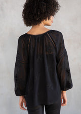 [Color: Black] A model wearing a dreamy sheer black chiffon blouse with floral embroidered details throughout. With long voluminous sleeves and lace trim.
