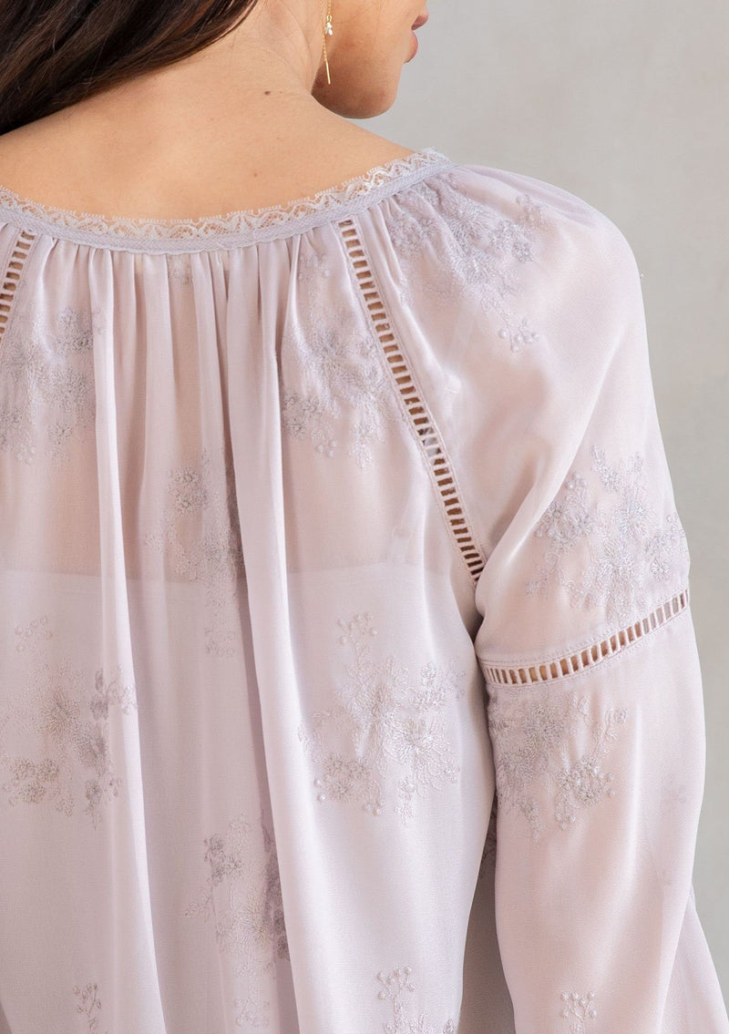 [Color: Dusty Mauve] A model wearing a dreamy sheer chiffon blouse with floral embroidered details throughout. With long voluminous sleeves and lace trim.