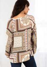 [Color: Ivory/Taupe] A model wearing a classic bohemian ivory and taupe peasant top in a trendy paisley patchwork print. With a button front, a split v neckline with tassel ties, and long voluminous sleeves. 