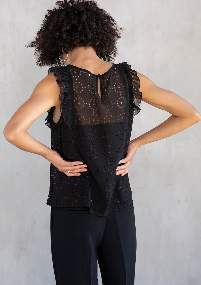 [Color: Black] A model wearing a black chiffon top with metallic laser cut detail. With a flutter cap sleeve and a back keyhole detail with button closure.