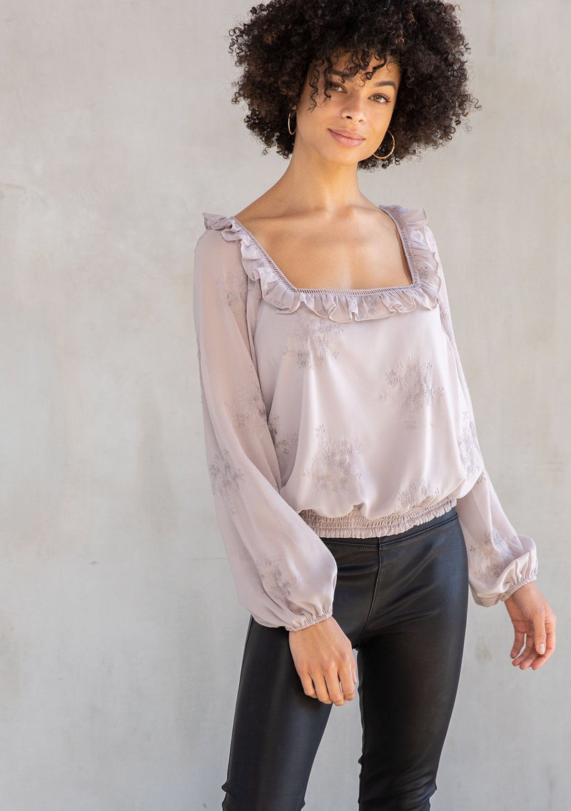 [Color: Dusty Mauve] A modal wearing a trendy light purple cropped bohemian top in floral embroidered chiffon. With a ruffle and lattice trimmed square neckline and voluminous long sleeves.