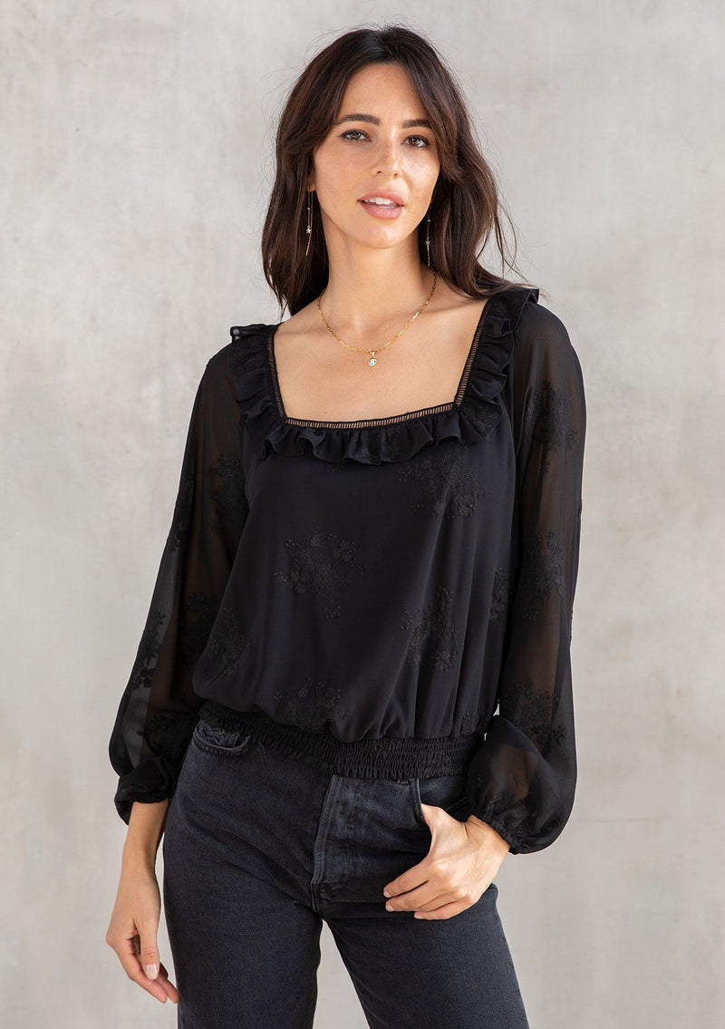 [Color: Black] A modal wearing a trendy black cropped bohemian top in floral embroidered chiffon. With a ruffle and lattice trimmed square neckline and voluminous long sleeves. 