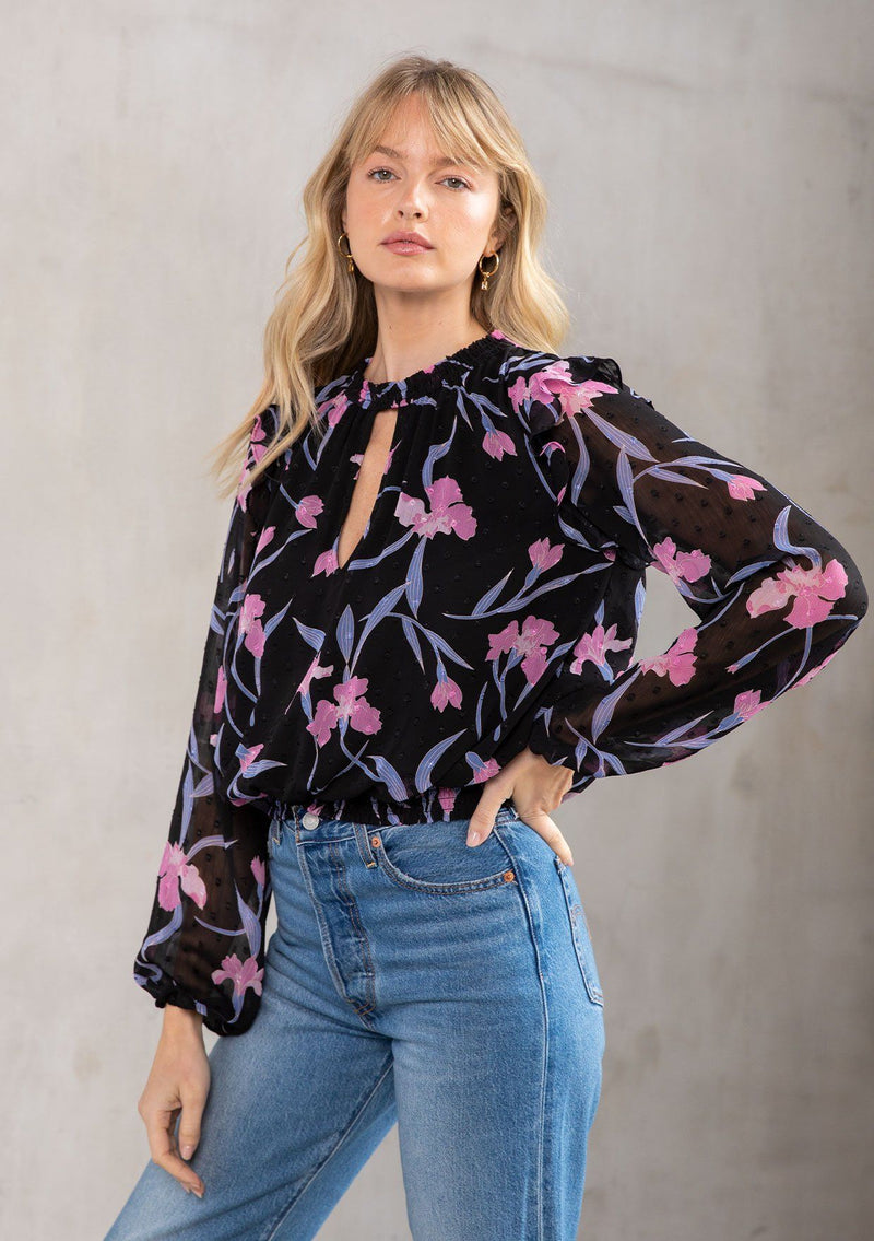 [Color: Black/Lilac] A model wearing an ultra pretty sheer floral blouse in black and lilac purple clip dot chiffon. With a front keyhole, long sheer sleeves, and a smocked high neckline. 