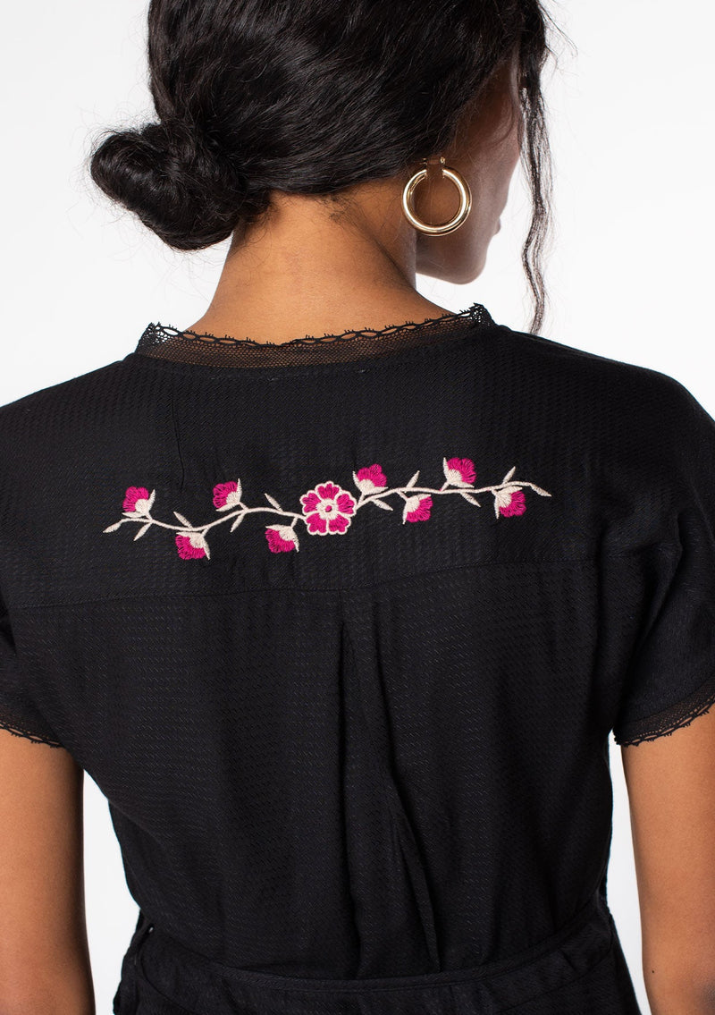[Color: Black/Mulberry] A model wearing a black bohemian wrap top with floral embroidery detail, lace trim, and short sleeves.