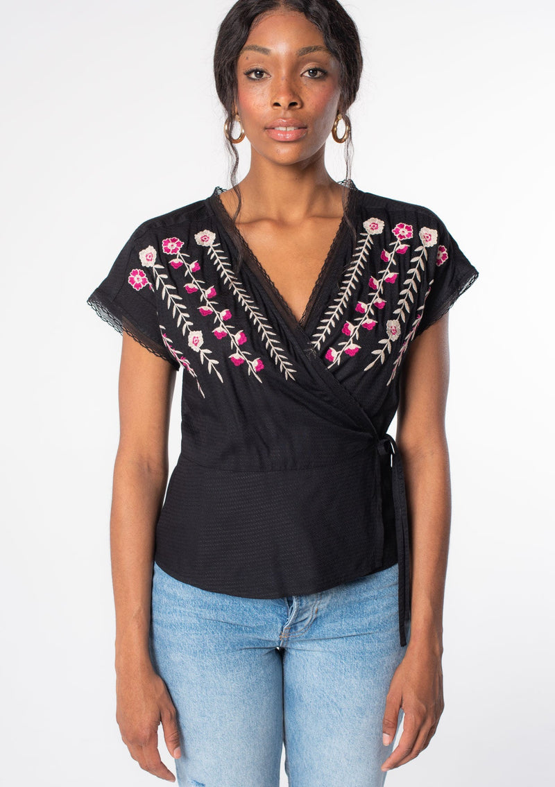 [Color: Black/Mulberry] A model wearing a black bohemian wrap top with floral embroidery detail, lace trim, and short sleeves.