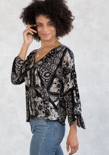 [Color: Black/Taupe] A model wearing a bohemian black and taupe bandana paisley print button front top. With a pretty self covered button front, tie wrist cuffs, and a flattering v neckline. 