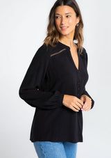 [Color: Black] A model wearing a timeless long sleeve black linen blend blouse. With a decorative button front, delicate lattice trim, and pleated details.