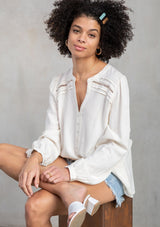 [Color: Vanilla] A model wearing a timeless long sleeve off white linen blend blouse. With a decorative button front, delicate lattice trim, and pleated details. 