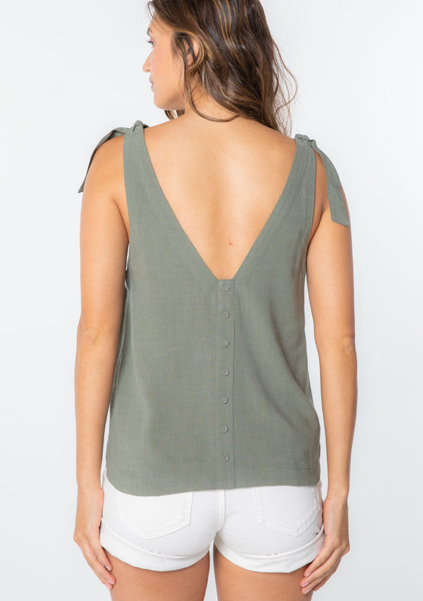[Color: Olive] A model wearing an olive green linen blend tank top with a tie shoulder and a button up back detail. 
