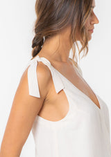 [Color: Vanilla] A model wearing an off white linen blend tank top with a tie shoulder and a button up back detail. 