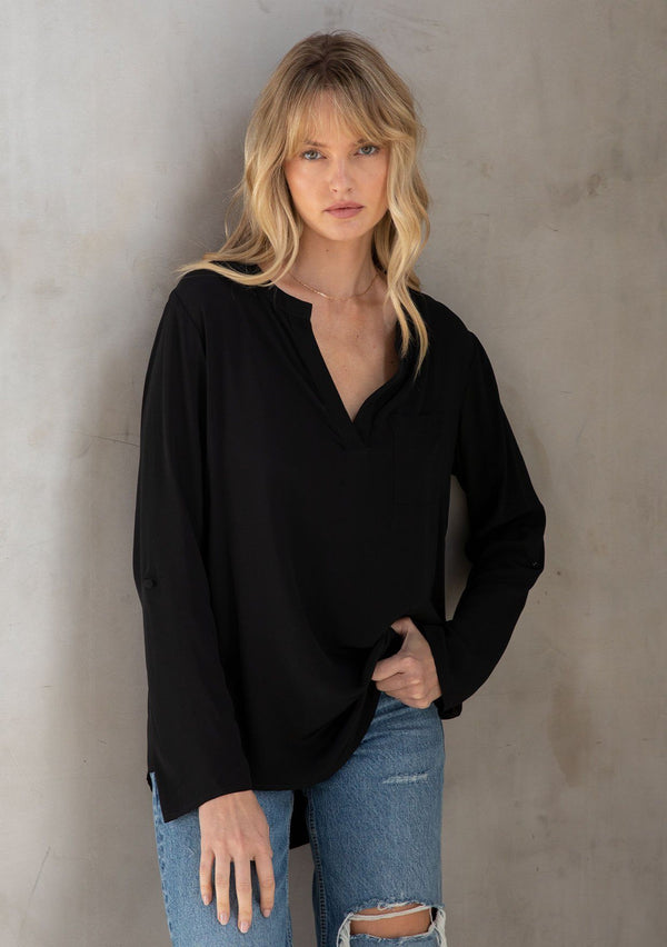 [Color: Black] A model wearing a silky black blouse with rolled tab sleeves, a front patch pocket, and a split v neckline. Classic top for the office. 