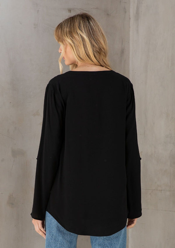 [Color: Black] A model wearing a silky black blouse with rolled tab sleeves, a front patch pocket, and a split v neckline. Classic top for the office. 