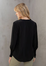 [Color: Black] A model wearing a classic black peasant top, designed in silky crepe. Featuring a split v neckline with ties and long voluminous sleeves.