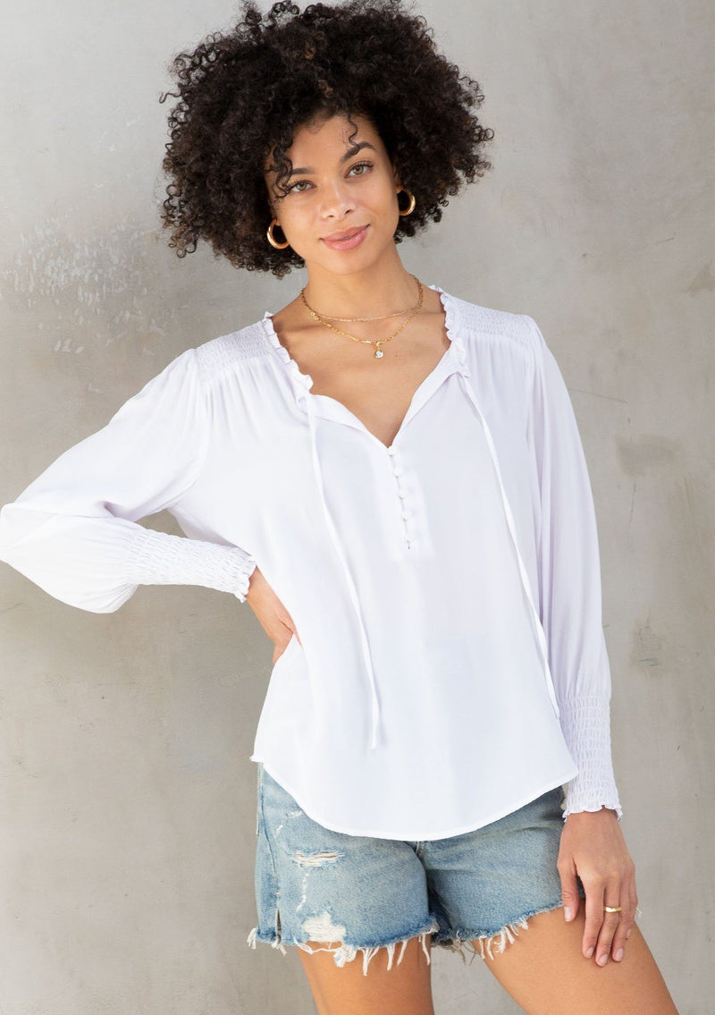 [Color: Chalk] A model wearing a classic white peasant top, designed in silky crepe. Featuring a split v neckline with ties and long voluminous sleeves.