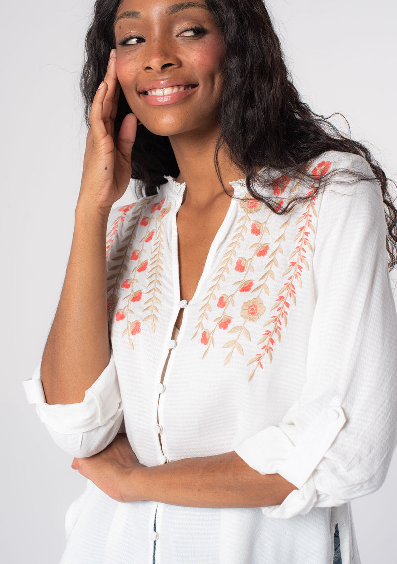 [Color: Ivory/Coral] A model wearing a soft white bohemian button front shirt with long rolled sleeves and floral embroidered details.