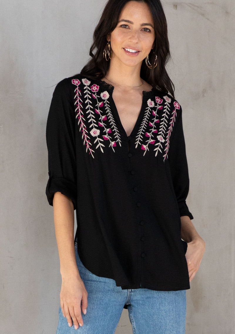[Color: Black/Mulberry] A model wearing a soft black bohemian button front shirt with long rolled sleeves and floral embroidered details. 