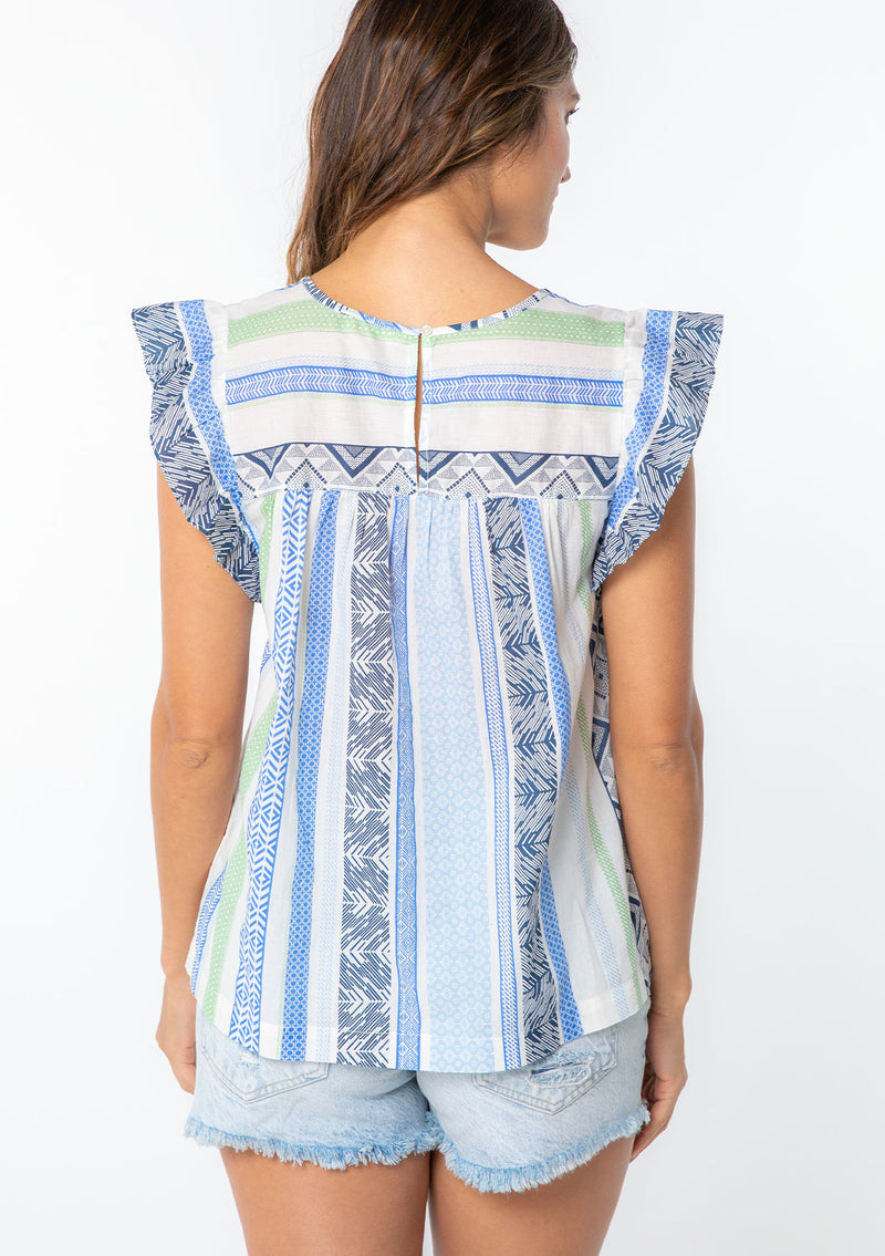 [Color: Blue/Sage] A model wearing a blue and white multi pattern stripe cotton bohemian top with a short ruffled cap sleeve. 