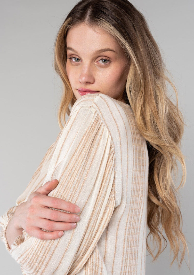 [Color: Natural/Tan] A close up side facing image of a blonde model wearing a resort ready bohemian top in a natural and tan stripe. With long sleeves, a v neckline, and a tie front waist. 