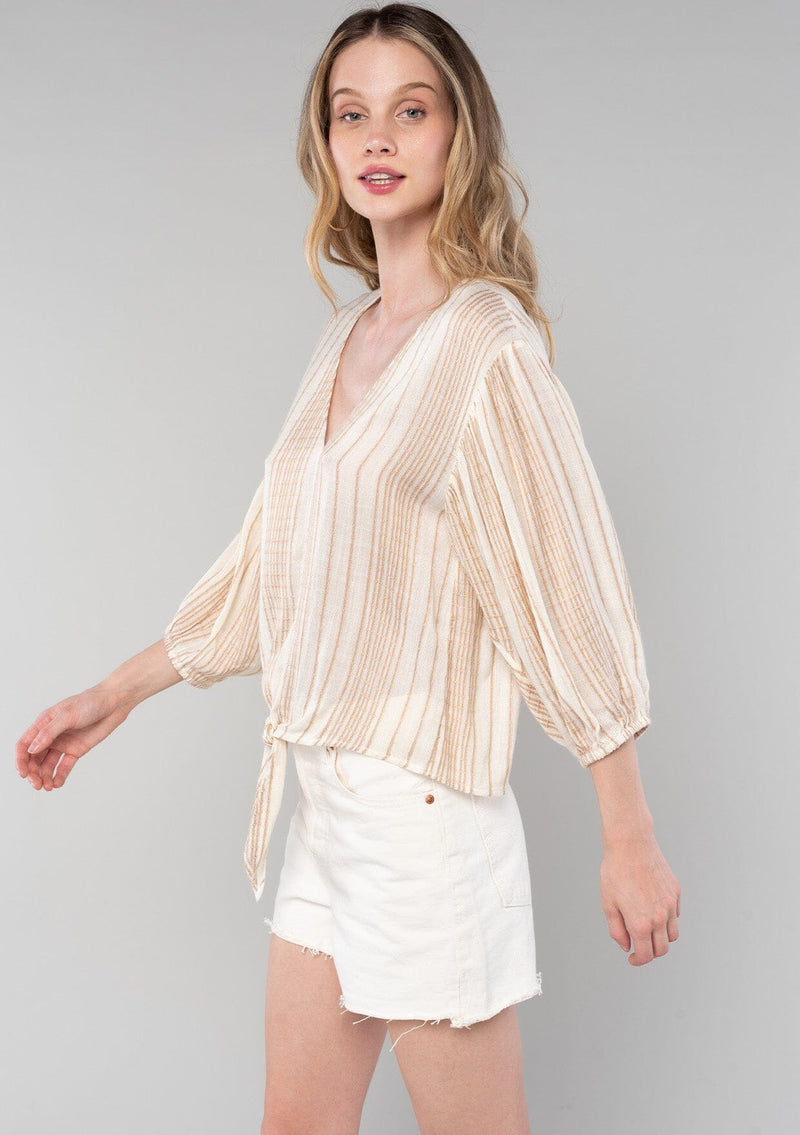 [Color: Natural/Tan] A side facing image of a blonde model wearing a resort ready bohemian top in a natural and tan stripe. With long sleeves, a v neckline, and a tie front waist. 