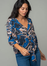 [Color: Cobalt/Tan] A front facing image of a brunette model wearing a navy blue and tan butterfly wing print top with three quarter length voluminous sleeves and a tie front detail. 