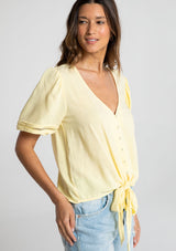 [Color: Daffodil] A model wearing a timeless yellow linen blend bohemian top. With short puff sleeves, an adjustable tie front waist detail, and a button front.