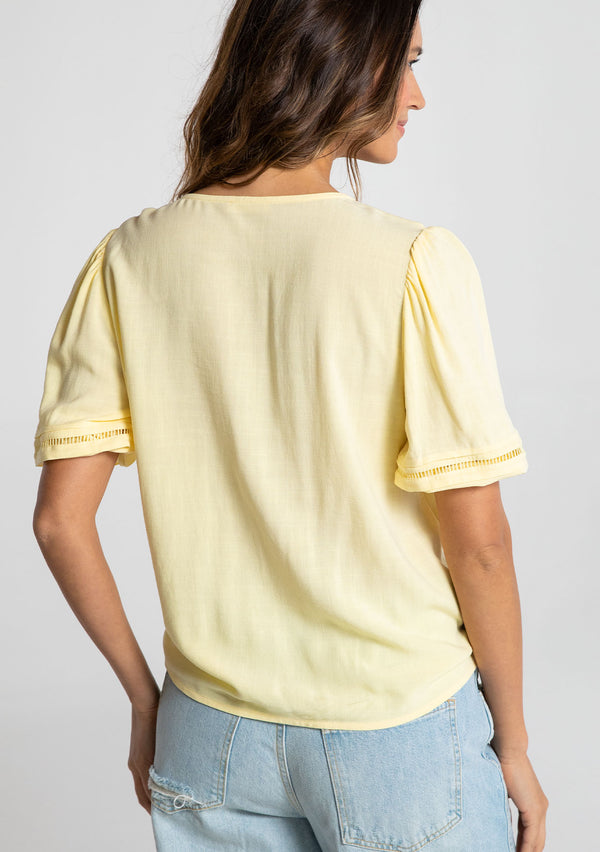 [Color: Daffodil] A model wearing a timeless yellow linen blend bohemian top. With short puff sleeves, an adjustable tie front waist detail, and a button front.