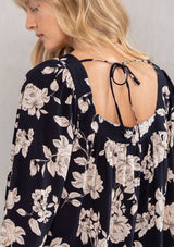 [Color: Black/Natural] A model wearing a flowy bohemian blouse in a black and natural floral print. With long voluminous sleeves, a trendy square neckline, and adjustable tie back detail.