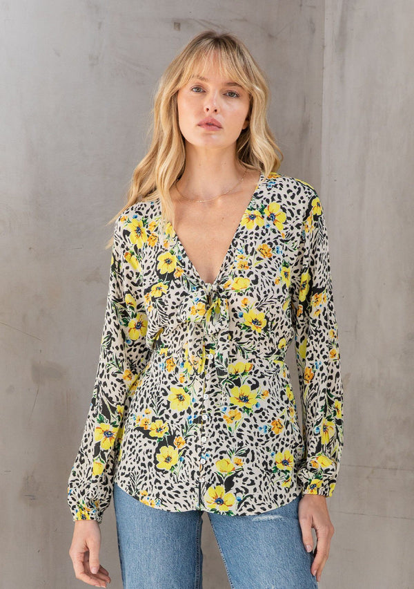 [Color: Ivory/Lemon] A model wearing a pretty yellow floral print top with a button front, long volume sleeves, and tie front detail. 