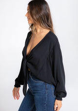 [Color: Black] A model wearing a flowy long sleeve black bohemian tie front top. 