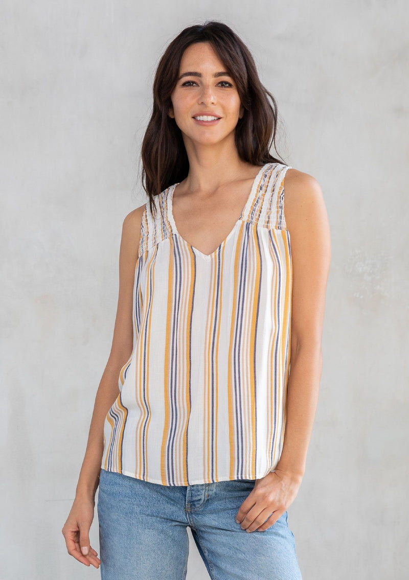 [Color: Dijon/Off White] A model wearing an ultra soft and lightweight Summer tank top in a white and yellow stripe. With a loose and flowy silhouette, a v neckline, and smocked yoke detail. 