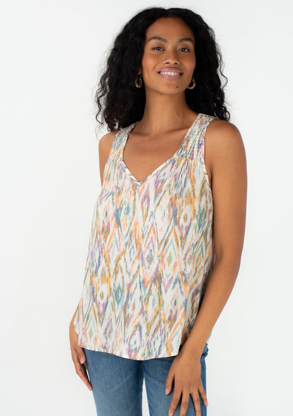 [Color: Natural/Teal] A front facing image of a brunette model wearing a casual resort tank top in a multi color bohemian diamond print. With a v neckline and a smocked yoke detail. 