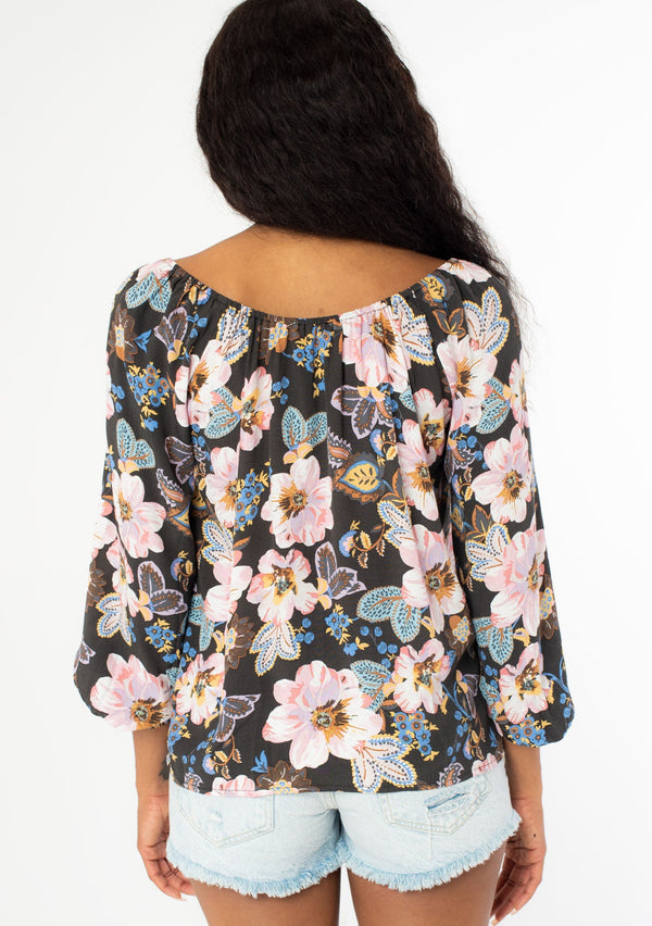 [Color: Charcoal/Rose] A back image of a black model with long wavy hair wearing a flowy bohemian top with long sleeves and a wide, round elastic neckline that can be worn on or off the shoulder.