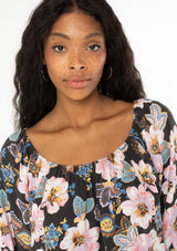 [Color: Charcoal/Rose] A close up image of a black model with long wavy hair wearing a flowy bohemian top with long sleeves and a wide, round elastic neckline that can be worn on or off the shoulder.