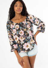[Color: Charcoal/Rose] A front facing image of a black model with long wavy hair wearing a flowy bohemian top with long sleeves and a wide, round elastic neckline that can be worn on or off the shoulder. 