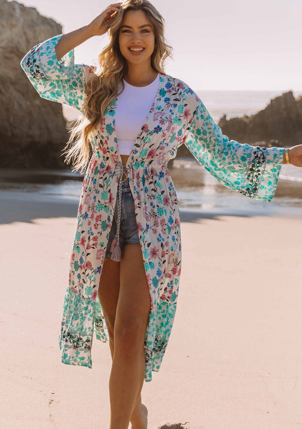 [Color: Jade/Berry] A model wearing a teal, white and pink floral print maxi kimono with long wide sleeves and a rope tie front.
