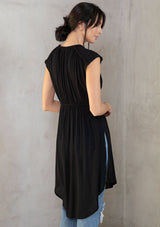 [Color: Black] A model wearing a floaty black bohemian sheer cap sleeve tunic top with button front and braided trim. 