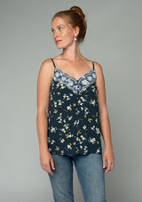 [Color: Navy/Powder Blue] A front facing image of a red headed model wearing a bohemian navy blue, yellow, and white floral print camisole tank top. With a lace trim v neckline, a self covered button front, and adjustable spaghetti straps. 