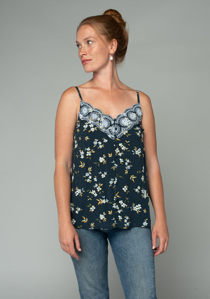 [Color: Navy/Powder Blue] A front facing image of a red headed model wearing a bohemian navy blue, yellow, and white floral print camisole tank top. With a lace trim v neckline, a self covered button front, and adjustable spaghetti straps. 