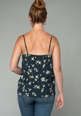 [Color: Navy/Powder Blue] A back facing image of a red headed model wearing a bohemian navy blue, yellow, and white floral print camisole tank top. With a lace trim v neckline, a self covered button front, and adjustable spaghetti straps. 