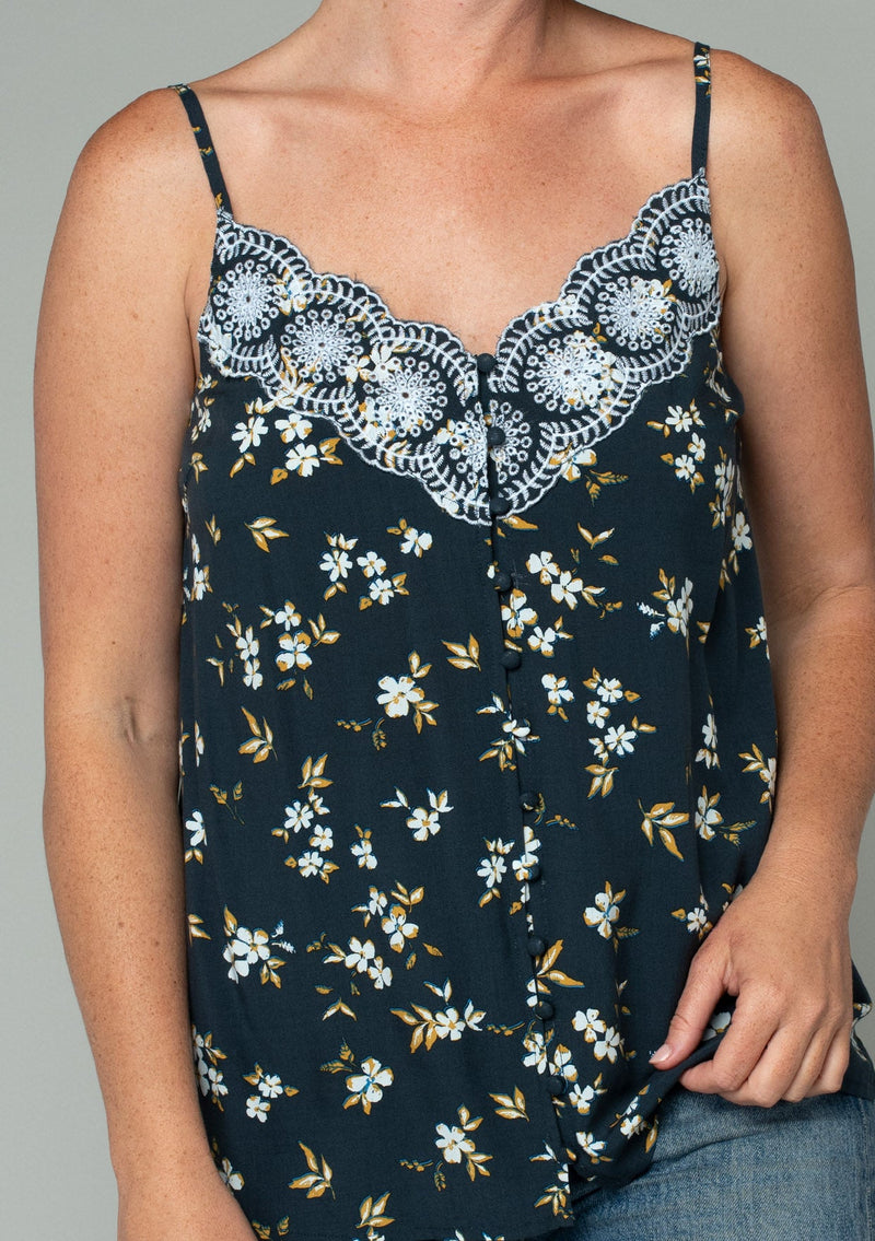 [Color: Navy/Powder Blue] A close up front facing image of a red headed model wearing a bohemian navy blue, yellow, and white floral print camisole tank top. With a lace trim v neckline, a self covered button front, and adjustable spaghetti straps. 