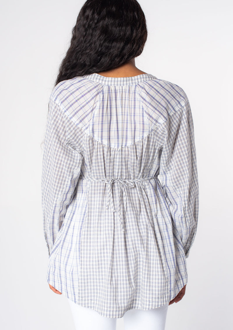 [Color: Natural/Blue] A model wearing an oversized tunic top in a blue and off white mixed plaid print, with long sleeves, and a cinched waist tie detail.