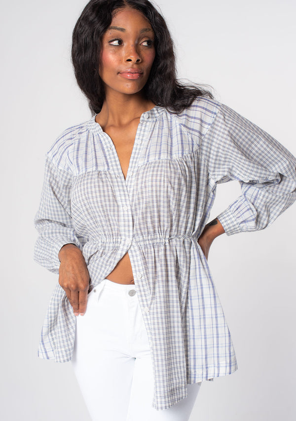 [Color: Natural/Blue] A model wearing an oversized tunic top in a blue and off white mixed plaid print, with long sleeves, and a cinched waist tie detail.