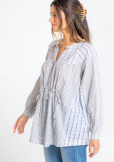 [Color: Natural/Blue] A model wearing an oversized tunic top in a blue and off white mixed plaid print, with long sleeves, and a cinched waist tie detail. 