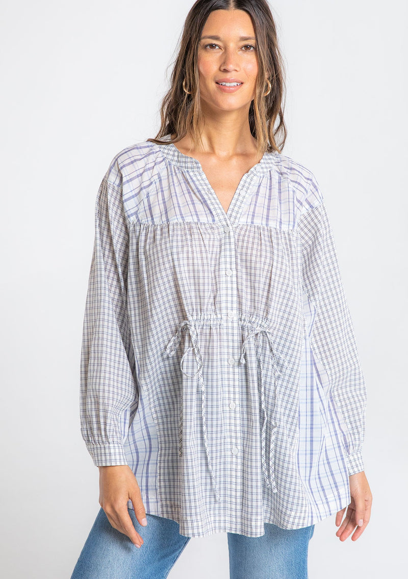 [Color: Natural/Blue] A model wearing an oversized tunic top in a blue and off white mixed plaid print, with long sleeves, and a cinched waist tie detail. 