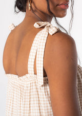 [Color: Tan/Natural] A model wearing a tan and white small checkered gingham print tank top with a tie shoulder detail.