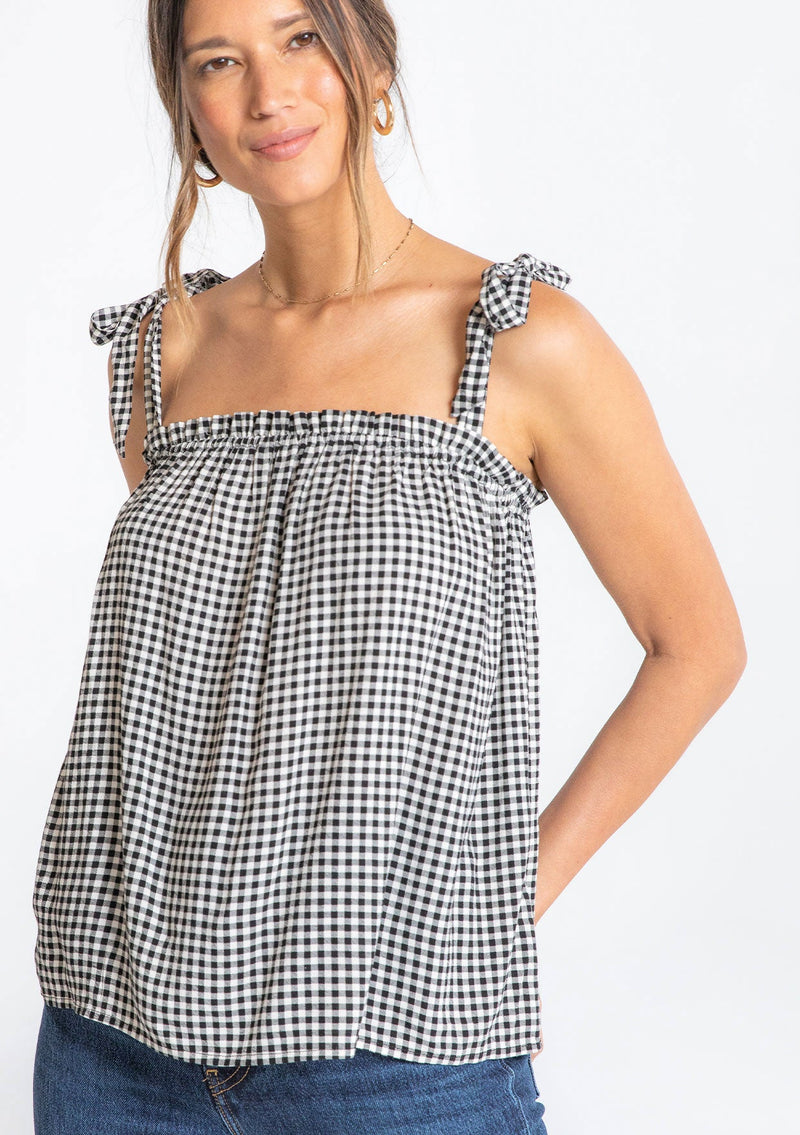 [Color: Black/Natural] A model wearing a black and white small checkered gingham print tank top with a tie shoulder detail. 