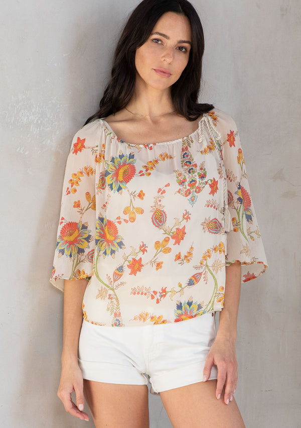 [Color: Ivory/Coral] A model wearing a flowy bohemian top in sheer chiffon. Designed in a floral print with a tassel tie drawstring neckline. 