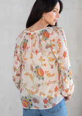 [Color: Ivory/Coral] A model wearing a sheer chiffon button front flowy bohemian top in a floral print. With long sleeves and ruffled trim. 
