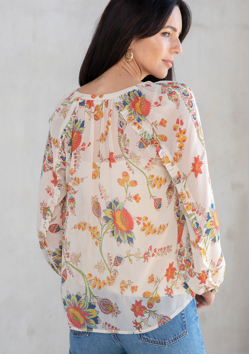 [Color: Ivory/Coral] A model wearing a sheer chiffon button front flowy bohemian top in a floral print. With long sleeves and ruffled trim. 